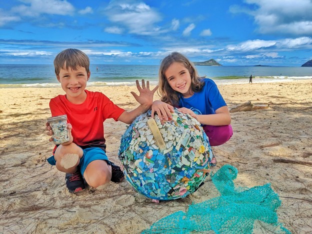 Two kids display their microplastic artwork using a washed up buoy and marine debris.