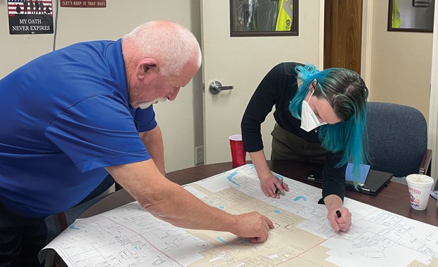 Two people pointing to and writing on a large paper map