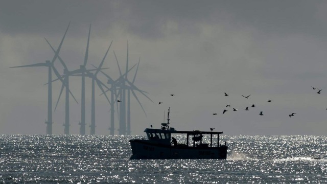 Fishing boast on the water in the foregroud surrounding by flying seagulls with wind turbines faded in the background