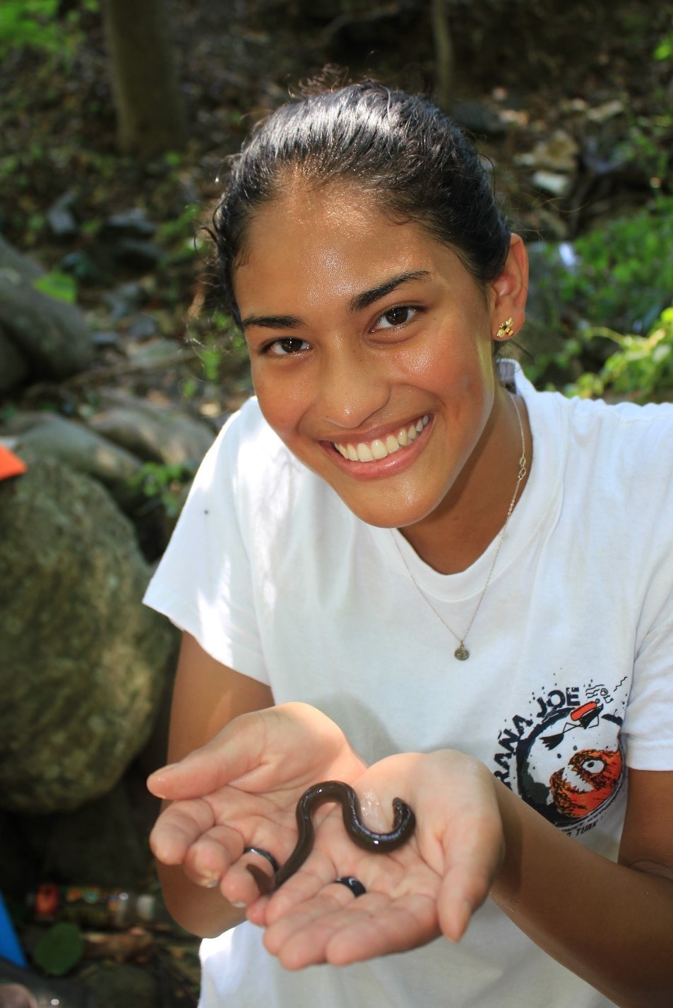 Person smiling at the camera holding a small eel in the palms of their hands.