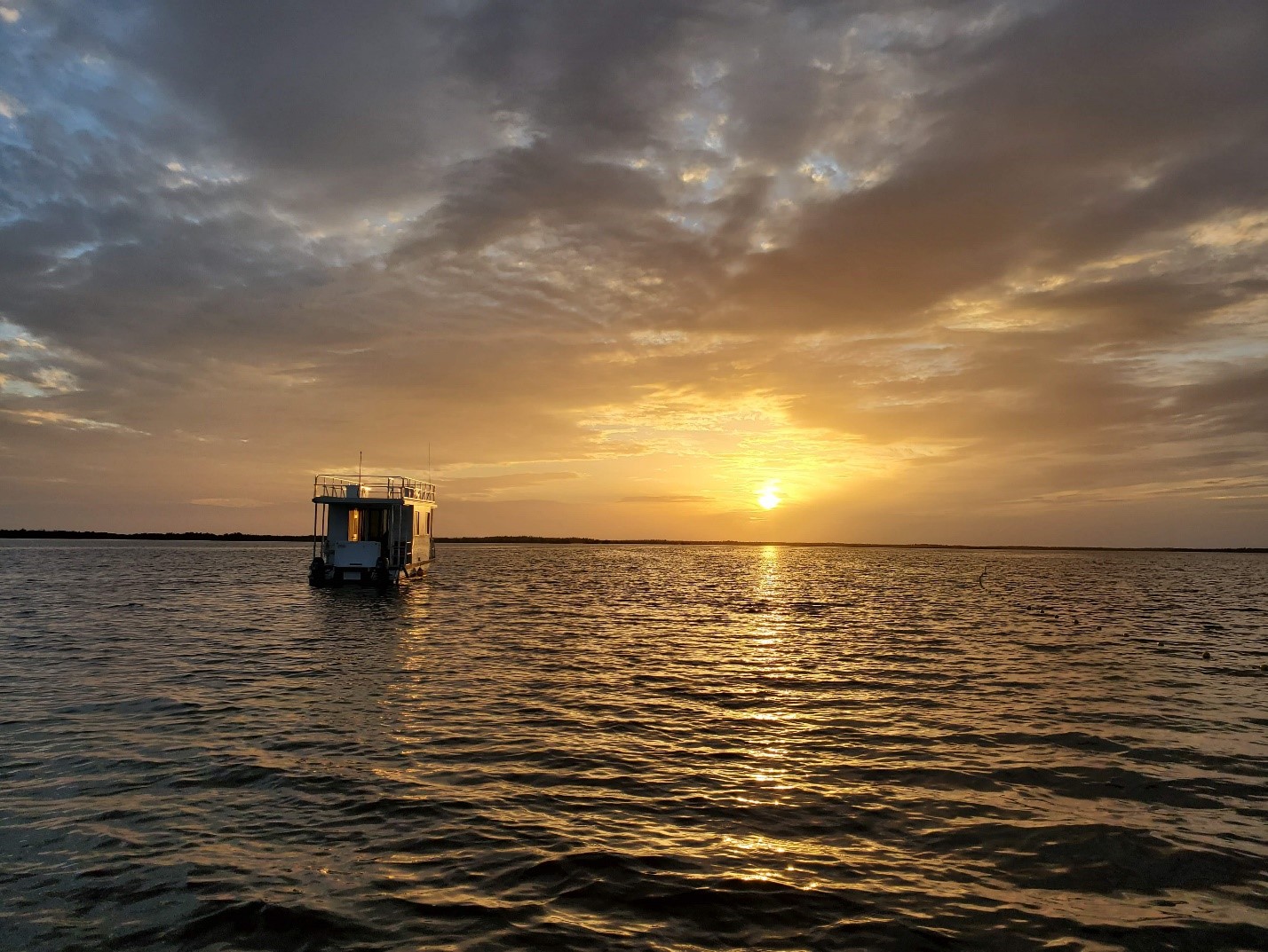 A boat floats in the water under a cloudy sunset.