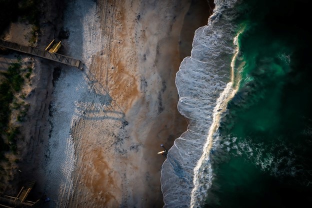Aerial view of a surfer walking on the beach, towards the waves.