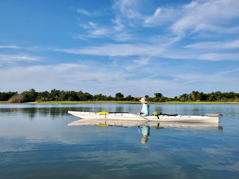 A person kayaking under a clear-blue sky with land in the distance.