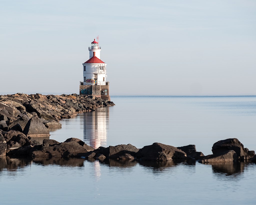 Large boulders surrounded by water lead to a red and white lighthouse.